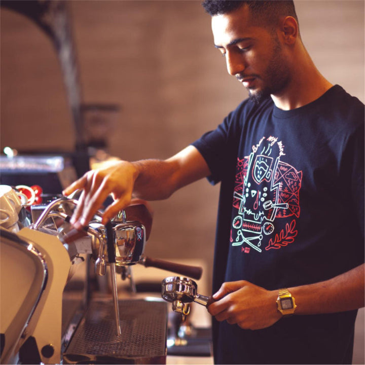 a professional Barista trainer in caffeinelab uniform making espresso holding a porta filter