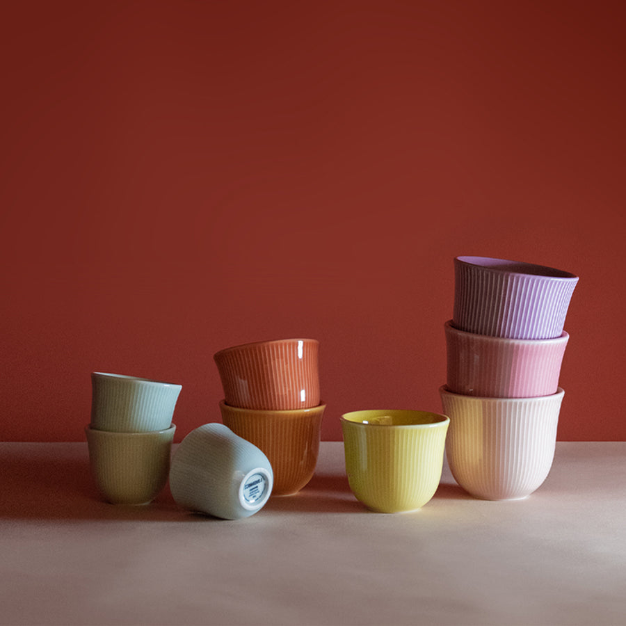 Loveramics Brewers Embossed Tasting Cups in green, blue, red, Purple and yellow colors. placed above each other on a marble table and a Burgandy red background.