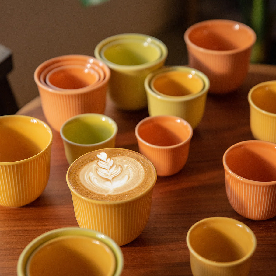 Loveramics Brewers Embossed Tasting Cups in orange and yellow color. placed a wooden table. one of them has a latte art on it