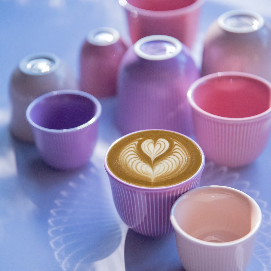 Loveramics Brewers Embossed Tasting Cups in pink and purple color. placed a mat table. one of them has a latte art on it