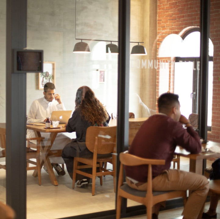 Two Customers having a meeting in a meeting room and other customer siting outside the room having a cup of coffee