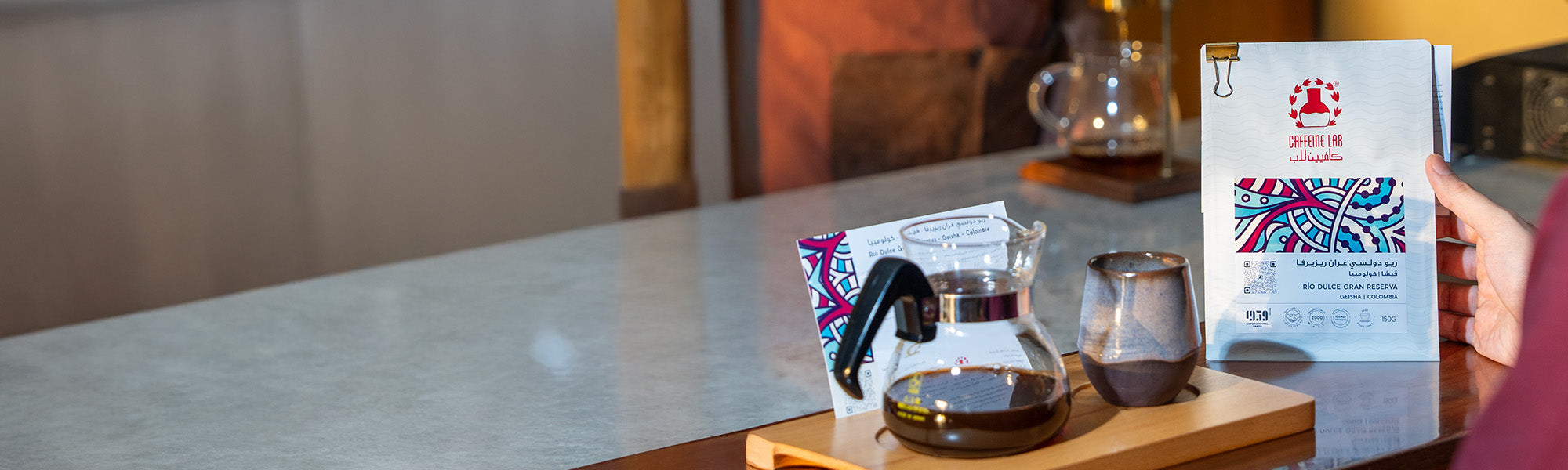 a Rio Dulce Colombia coffee beans bag held on a table. next o it a brewed or filtered coffee and its mug next to it